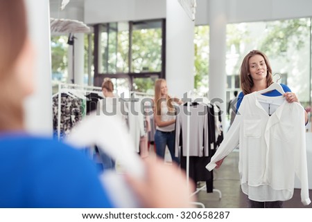 Stylish Young Woman Checking Out White Shirt In Front of a Mirror Inside a Clothing Store.