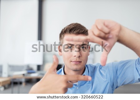 Close up Gorgeous Young Businessman In his Office, Looking at the Camera While Making a Hand Frame Gesture.