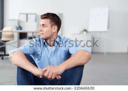 Pensive Young Office Man Sitting on the Floor with Arms Leaning on his Knees and Looking Into Distance.