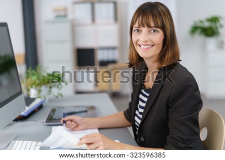 Half Body Shot of a Happy Businesswoman Working on Business Documents at her Table, Smiling at the Camera.