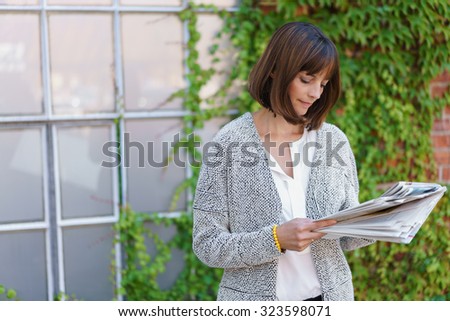 Businesswoman standing outside the window of a building with a green creeper on the wall reading documents in files she is holding with a serious expression