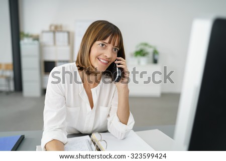 Happy Businesswoman at her Table, Talking to Someone Using her Mobile Phone