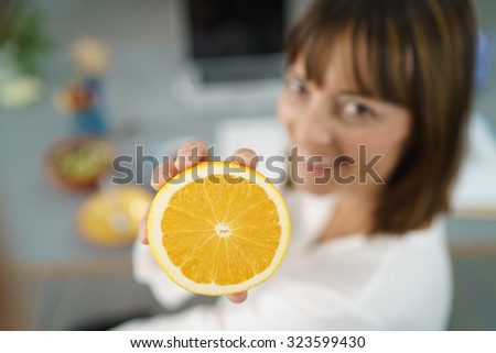 Happy Office Woman at her Desk Showing a Fresh Sliced Orange at the Camera in Close up.
