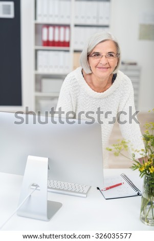 Thoughtful Middle Aged Businesswoman Leaning Against her Desk In the Office and Looking Into the Distance.