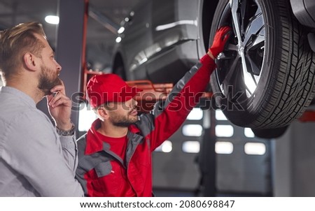 Side view of professional male technician explaining problem for customer and touching wheel of broken automobile in repair service Foto stock © 