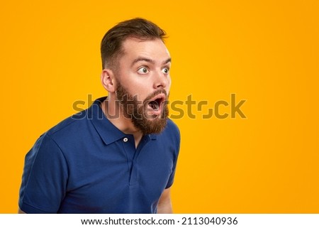Astonished bearded man in blue t shirt looking away with opened mouth against yellow background Foto d'archivio © 