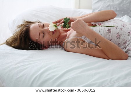 young woman lies on bed and smells a rose