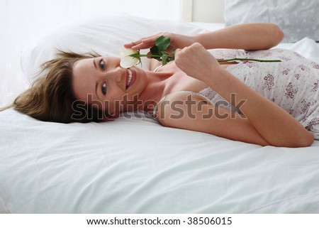 young woman lies on bed ans smells a rose