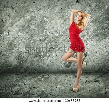 Full Length Portrait of a Sexy Blonde Woman in Red Fashion Dress against Concrete Wall
