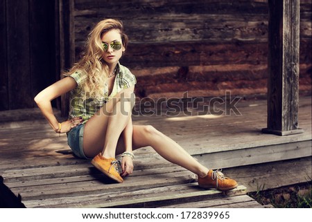 Trendy Hipster Girl Sitting on the Wooden Porch. Toned Photo. Modern Youth Lifestyle Concept.