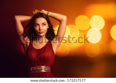 Portrait of a Beautiful Young Woman in Fashionable Red Dress over Bright Night Lights. Nightlife Party Concept.
