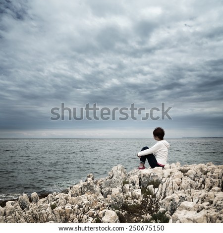 Lonely Woman Sitting at Stormy Sea. Toned and Desaturated Photo with Copy Space. Solitude Concept.
