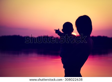 Silhouettes of Father and Baby Watching Sunset by the Lake.  Family Concept. Toned Photo with Copy Space.