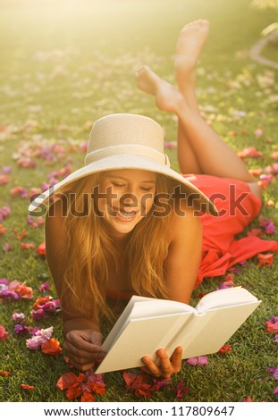 Beautiful Young Woman Reading a Book Outside on the Grass