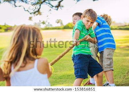 Group of Happy Young Children Playing Tug oF War Outside on Grass