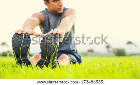 Attractive fit young man stretching before exercise, sunrise early morning backlit. Shallow depth of field, focus on shoes