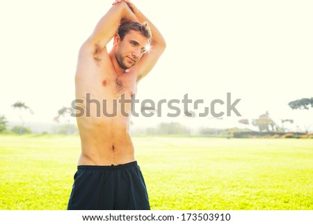 Attractive fit young man stretching before exercise workout, sunrise early morning backlit. Healthy lifestyle sports fitness concept.