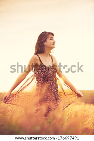 Beautiful young woman outdoors. Romantic Model in Sun Dress in Golden Field at Sunset. Happy Emotions, Glowing Sunlight. Backlit. Warm color tones