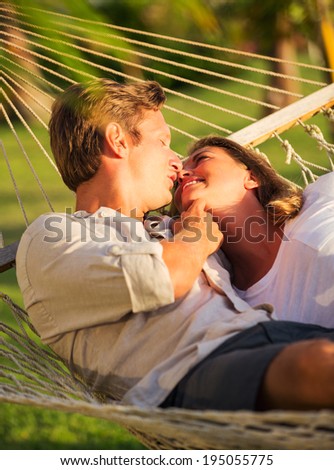 Romantic couple relaxing in tropical hammock at sunset