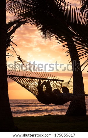 Silhouette of Romantic couple relaxing in tropical hammock at sunset