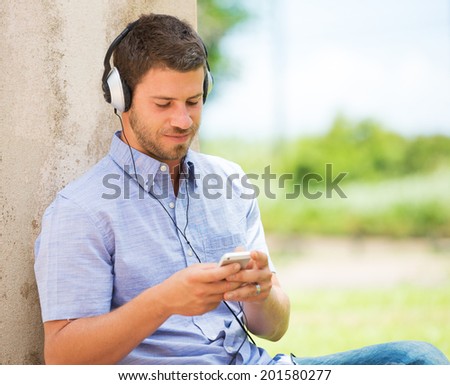 Young man using cell phone and head phones outside