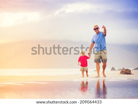Happy father and son walking on the beach at sunset holding hands