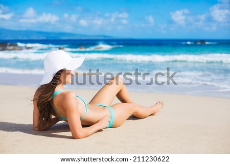 Beach vacation. Beautiful young woman in sun hat relaxing on the beach.