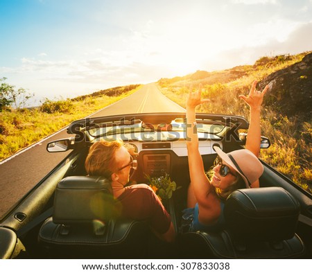 Happy Young Carefree Couple Driving Along Country Road in Convertible at Sunset