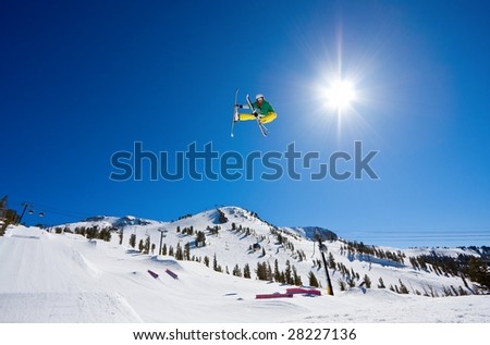 Skier Gets Radical Big Air with Sun and Blue Sky and Mountain In the Background