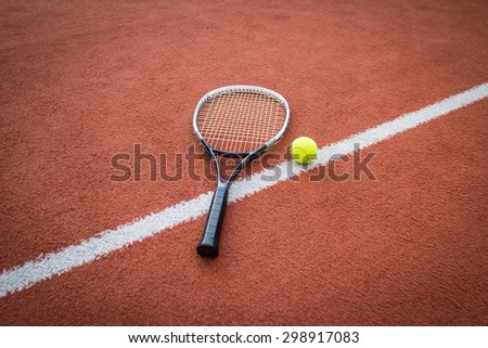 A black and white tennis racket near a yellow ball on a brick red court