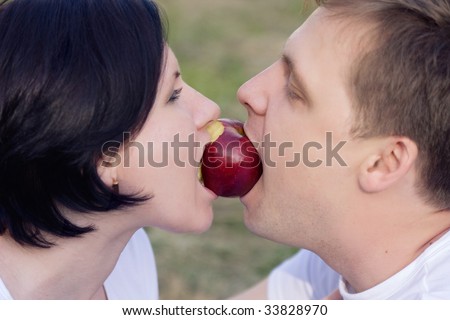 The young man and the young woman bite a red apple