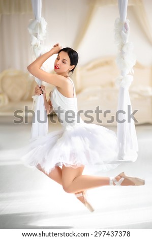 Beauty brunette ballerina on a swing in room, with ballet skirt and corset