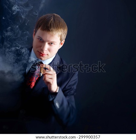 The man in suit smoke a cigar, looks at us. lots of smoke. A dark background
