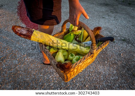 woman waved basket with vegetables accompanied with large knife, outdoor shot at sunset