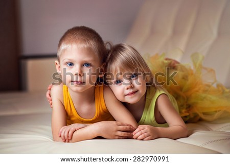 brother and sister lying on his stomach on a leather couch beside him and look at the camera