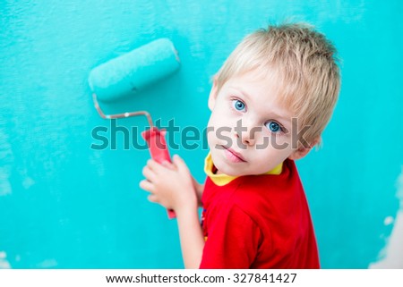 Cute blue-eyed blond pretty boy of five years in the red t-shirt makes repair paints the wall in blue roller