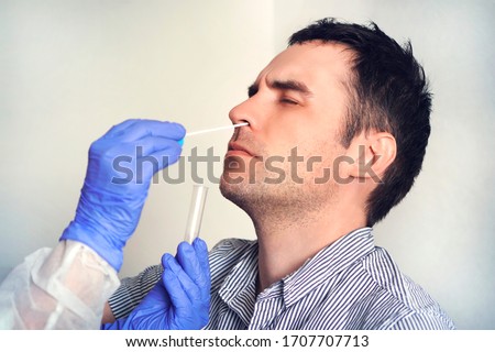 A doctor in a protective suit taking a nasal swab from a person to test for possible coronavirus infection. Nasal mucus testing for viral infections.