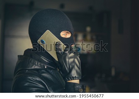 Young adult in black clothes with hidden face. Ill-intended fraudster uses mobile. Fraudster calls. Mobile racket. Hacker hijacks by phone. Cellphone account fraud. Scam 商業照片 © 