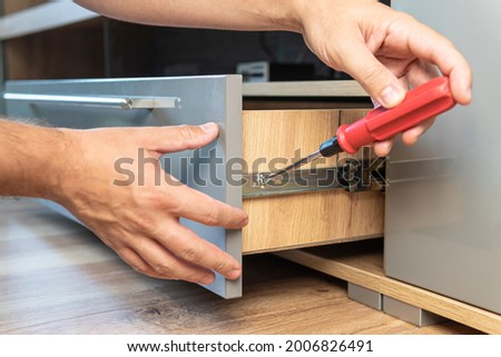 Young Handyman In Overall Installing Drawer In Kitchen. The man adjusts the drawer. Self-assembly of furniture. Photo stock © 