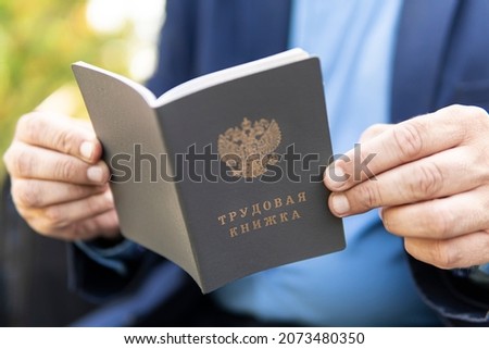 Work record book in a man hand. A businessman or an employee looks at document. The inscription in Russian is a work book