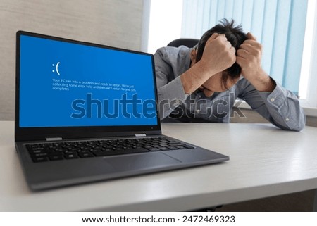 showing error blue screen on the Laptop against the background of an angry upset man clutching his head