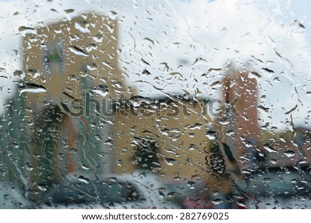 raindrops on glass, blurred in the background blue sky which stands back clear after the rain, and some buildings and cars, winter weather or summer storm?
