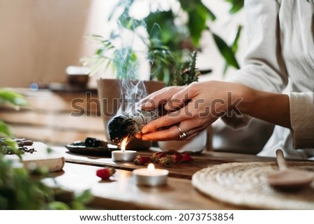 Woman hands burning white sage, palo santo before ritual on the table with candles and green plants. Smoke of smudging treats pain and stress, clear negative energy Stock fotó © 