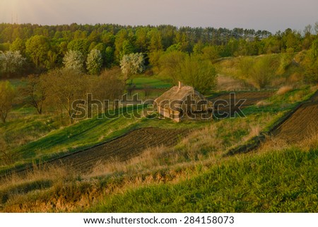 Agricultural land near old abandoned wooden house in Ukraine. Rural landscape in the morning. View on ploughed land plot on hills in spring
