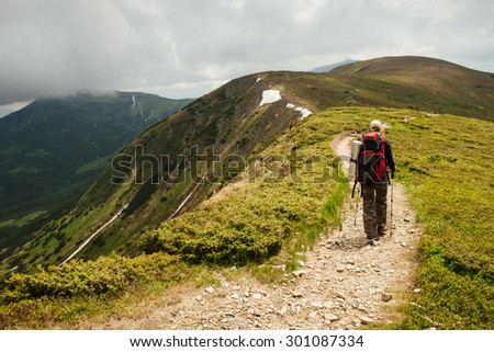 Nordic walk on the mountain road. Woman with trekking sticks under the clouds