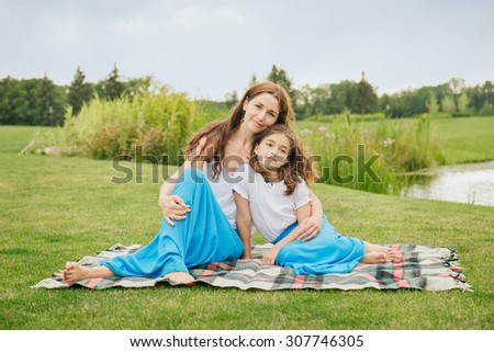 Mother with young daughter hugging on the grass in the park near lake. Family dressed the same clothes