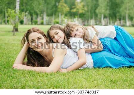 Mother with kids spending free time playing outdoors. Family has the same clothes. Children lie on mom\'s back