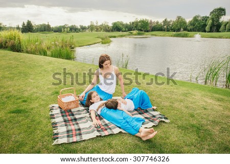 Mother with young daughters on picnic near the lake. Family relaxing in the same clothes outdoors.