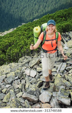 Women hiking with backpack holding trekking sticks high in rocky mountains in summer. Nordic walk.