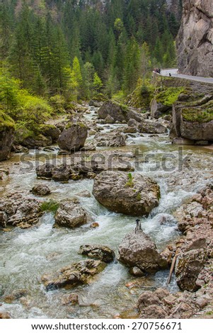 The picturesque mountain river with boulders at the foot of the cliff to the road. It is in the Carpathian Mountains, Romania, Transylvania.